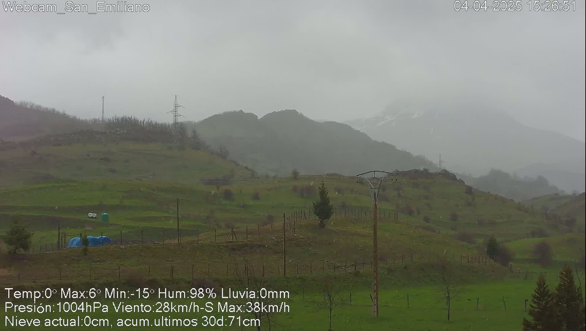 A rain-swept view of rolling green hills and distant mountains under a gray sky.