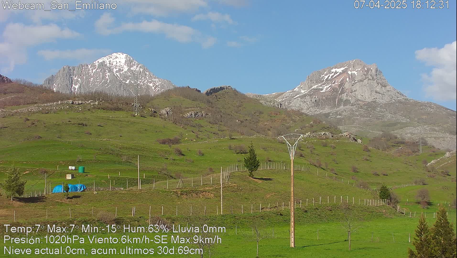 Two snow-capped mountains rise in the distance above a gently sloping green pasture under a mostly clear blue sky.