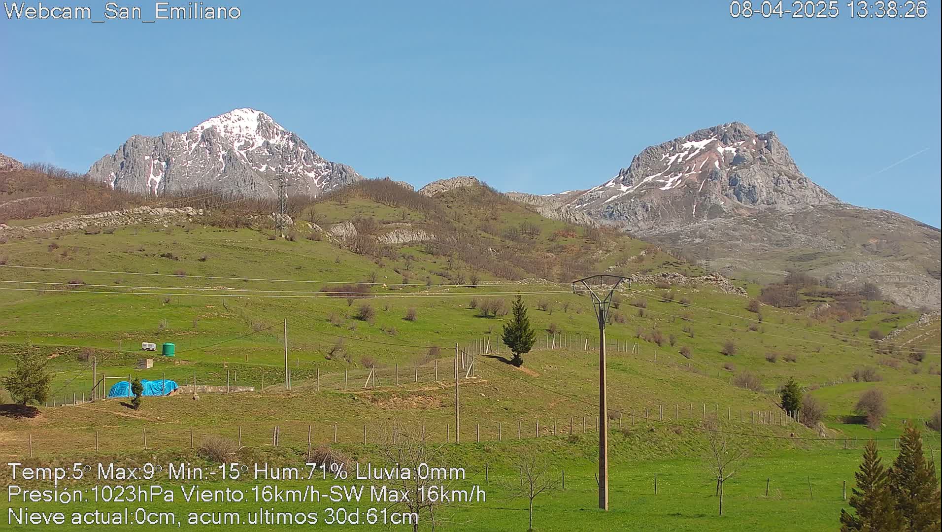 Two snow-capped mountains rise in the distance above a green, hilly landscape under a clear blue sky.