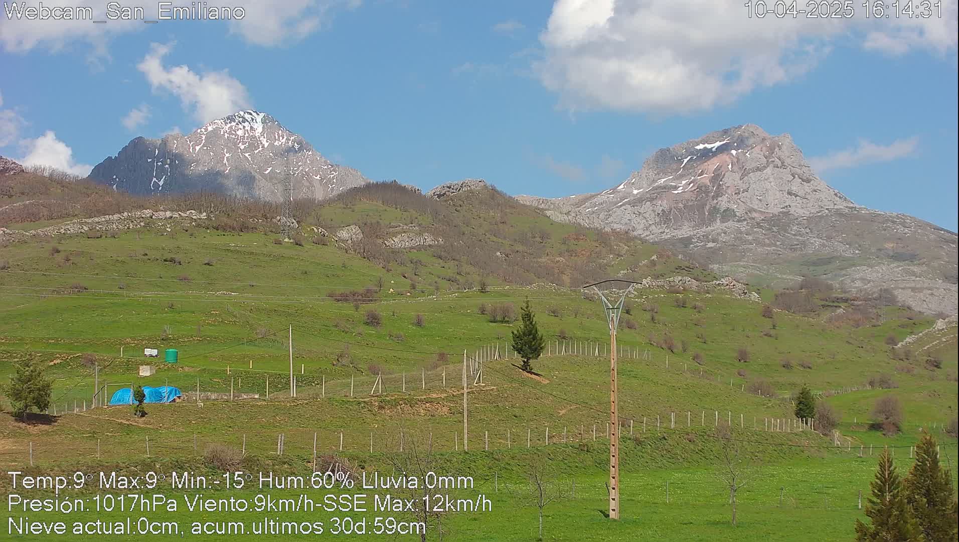 A green, hilly landscape with snow-capped mountains in the background under a mostly clear blue sky.