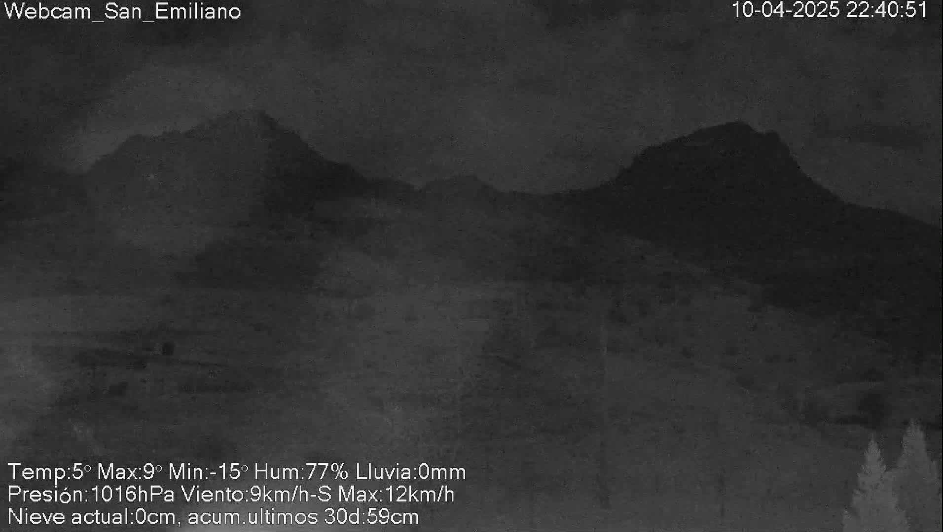 A nighttime, low-light view of dark mountains under a cloudy sky with light rain.