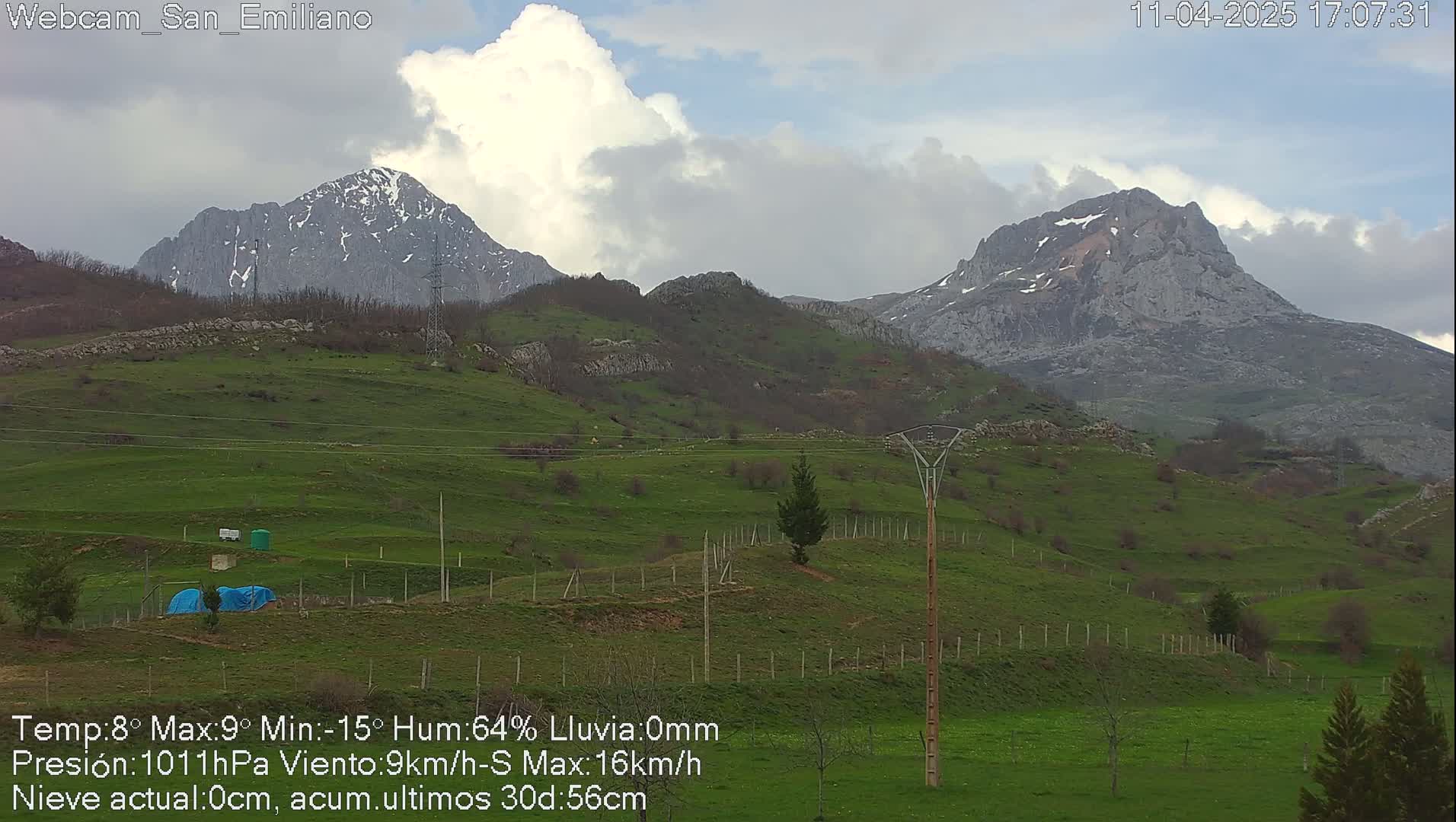 Two snow-capped mountains rise above a gently sloping green hillside under a cloudy sky.