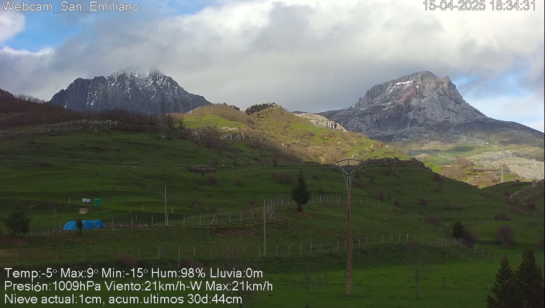 Rolling green hills and snow-capped mountains are visible under a partly cloudy sky.