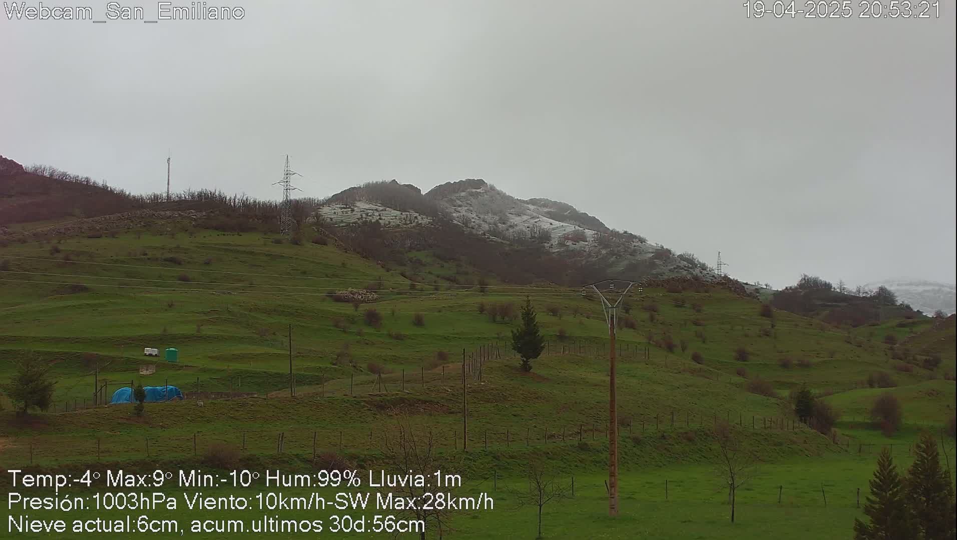 A mostly cloudy, rainy day reveals rolling green hills with a snow-dusted mountain in the background.