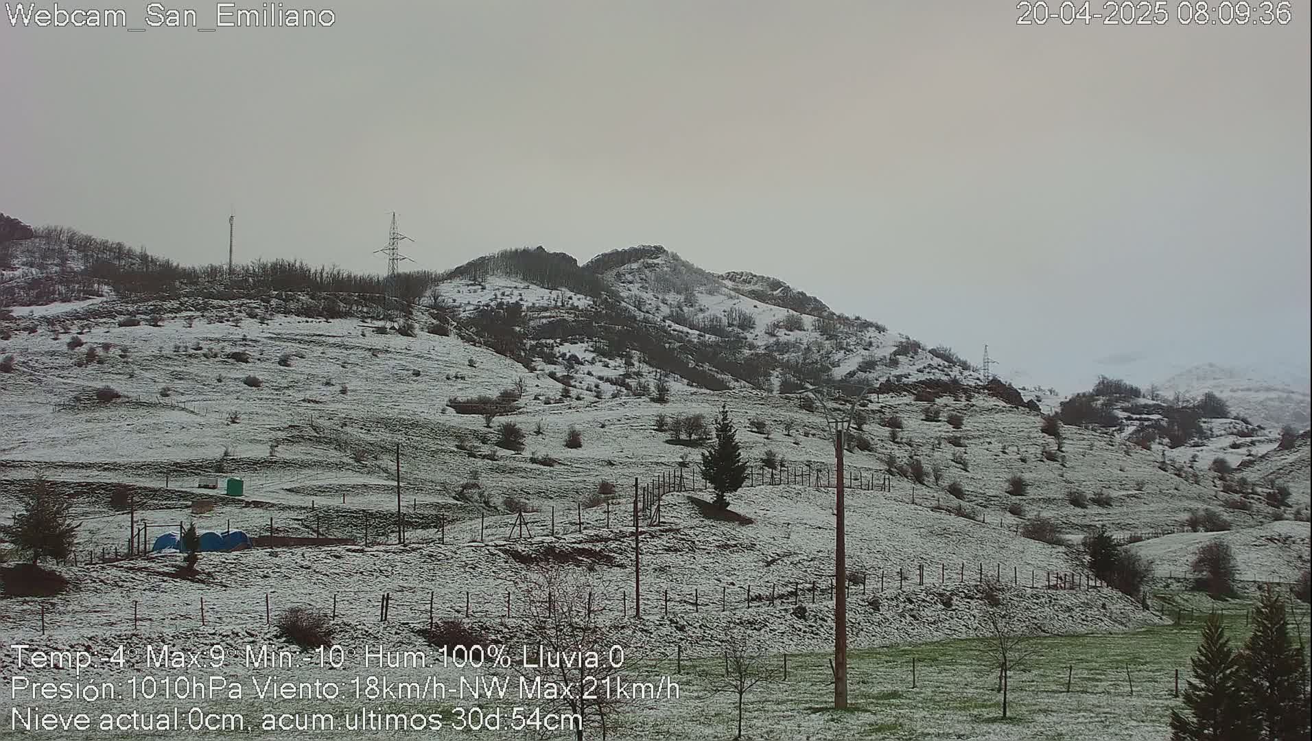 A snow-dusted landscape of rolling hills and sparse trees under a gray sky.