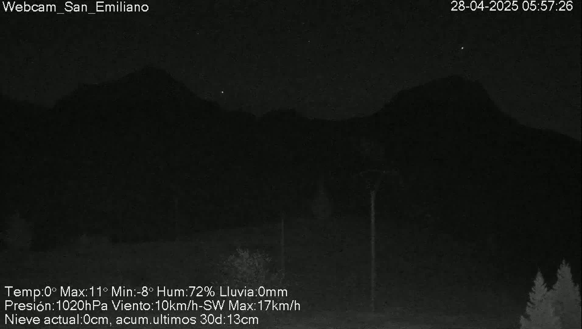 A nighttime, low-light image shows dark, silhouetted mountains under a mostly clear night sky with a few visible stars; there is no precipitation.