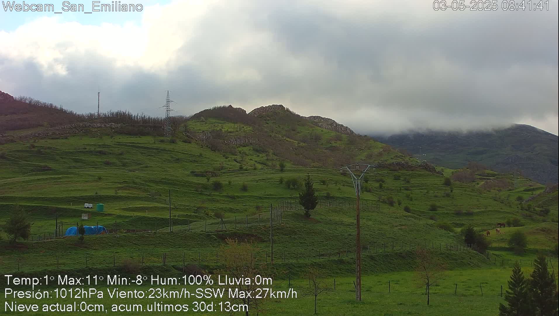 A view of rolling green hills under a cloudy sky, with some low-lying fog in the distance.