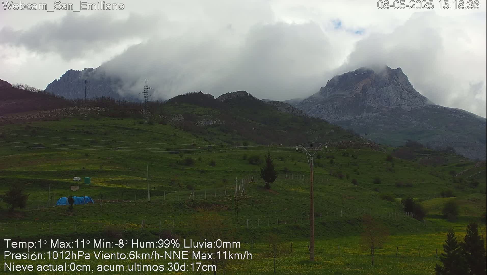 A cloudy day reveals a green hillside leading to a large, partially cloud-covered mountain.