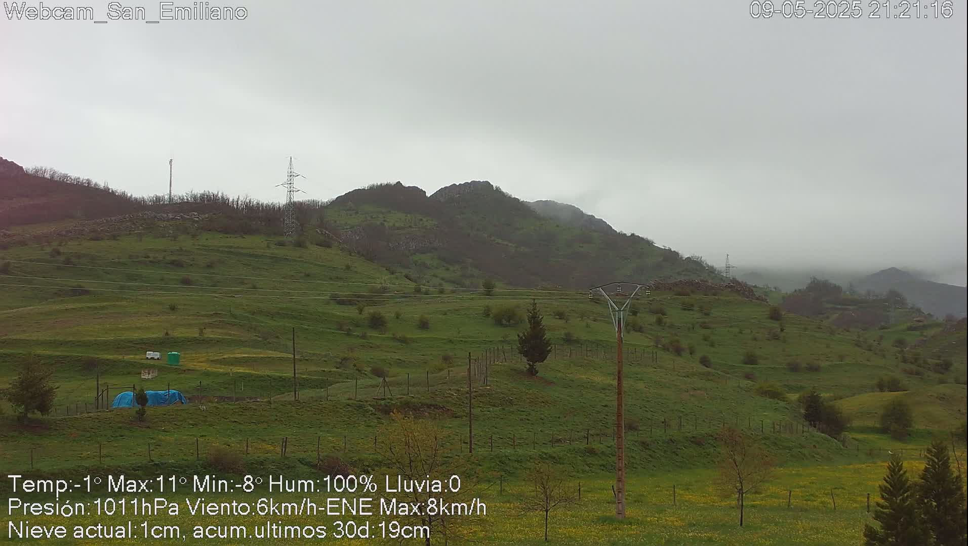 A misty, overcast day reveals rolling green hills and a power line against a backdrop of mountains.