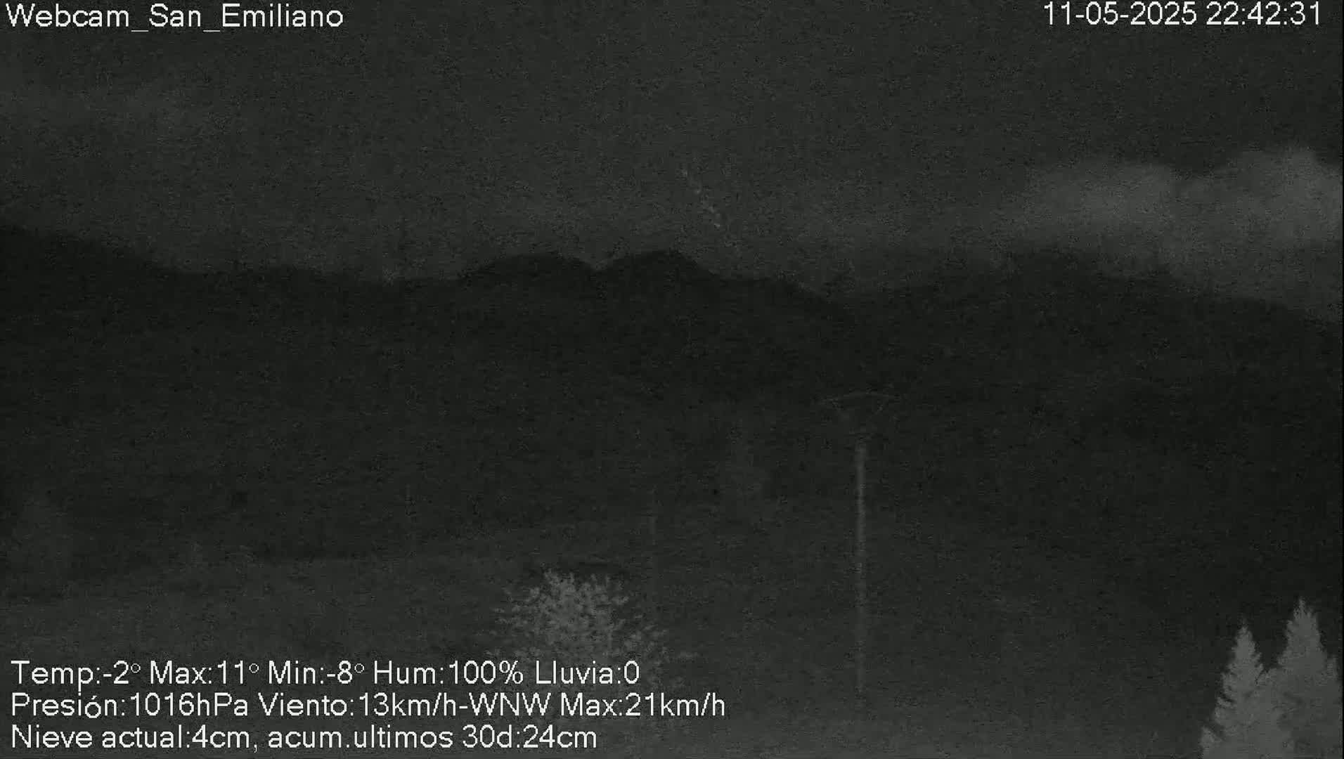 A nighttime, low-light view of dark mountains under a cloudy sky with snow on the ground.