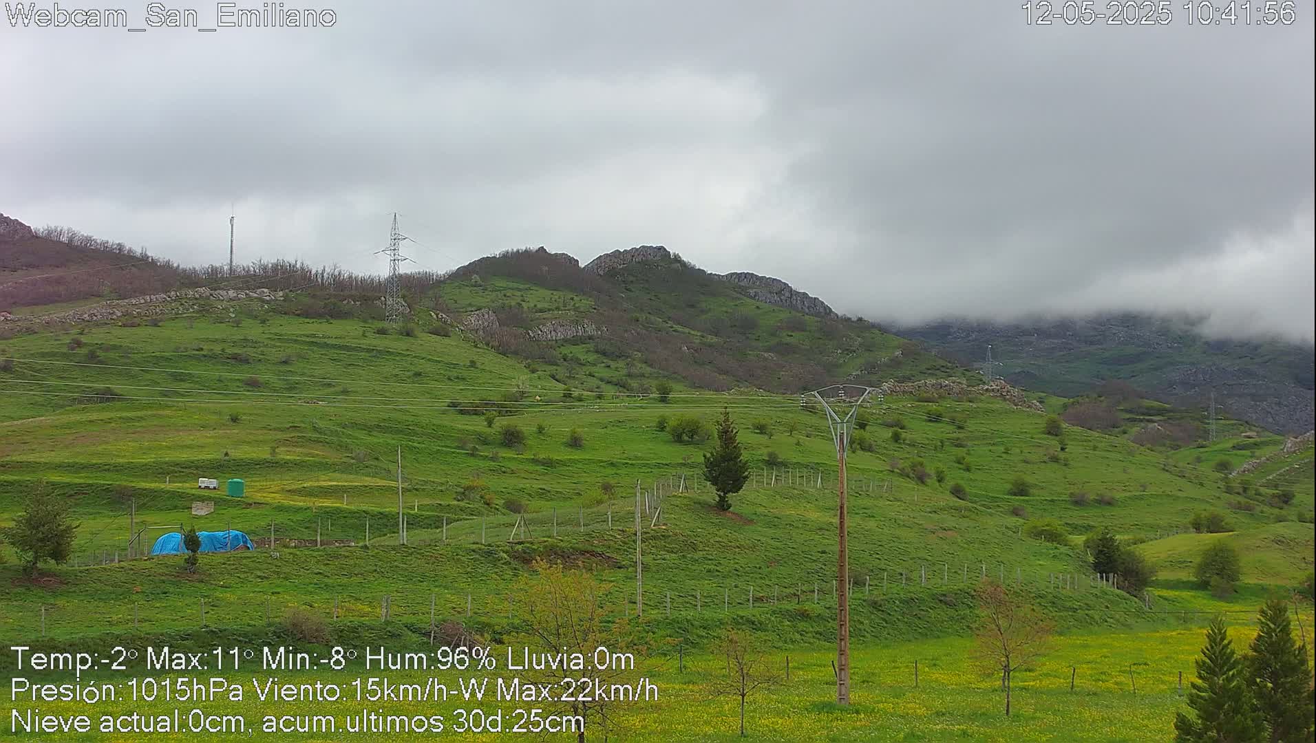 A green, hilly landscape under a cloudy sky, with power lines running through it.