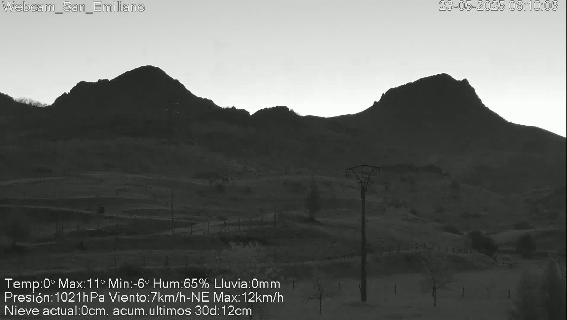 A grayscale image shows two dark, mountainous silhouettes against a pale, dawn sky; a single utility pole stands in the foreground of the valley.