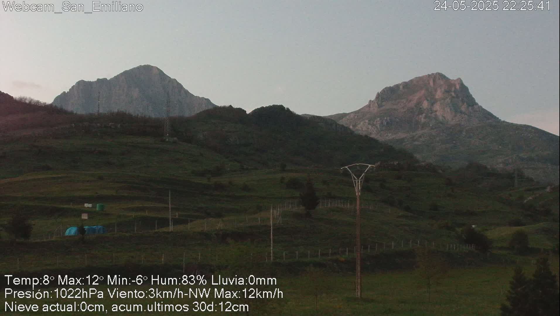 Two mountain peaks are visible in the distance under a twilight sky, with a grassy field and utility poles in the foreground.