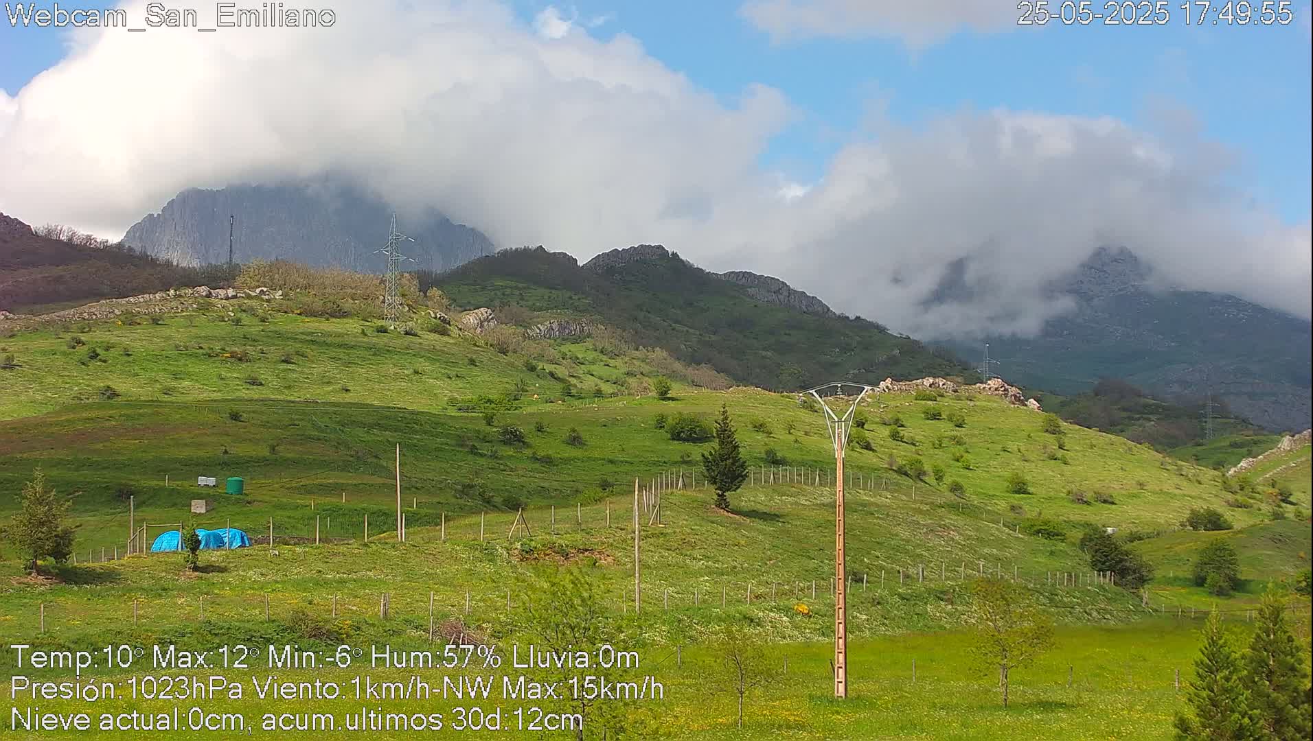 A partly cloudy day reveals rolling green hills and mountains partially obscured by clouds.