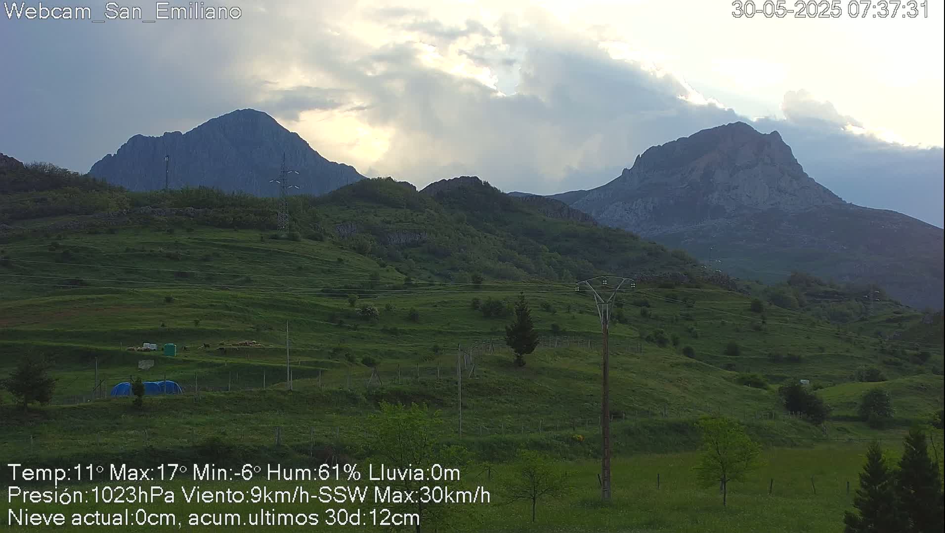 Two mountain ranges are visible under a cloudy sky, with a lush green valley in the foreground.