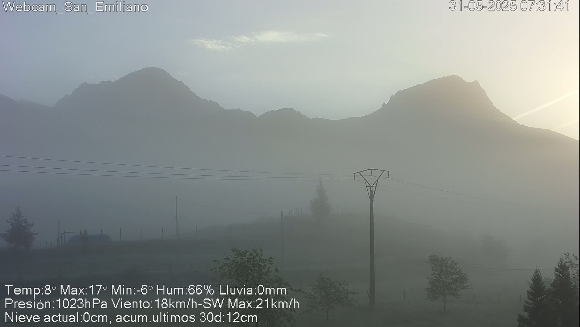 A foggy sunrise reveals a mountain range in the distance, with a lone electricity pylon in the foreground.