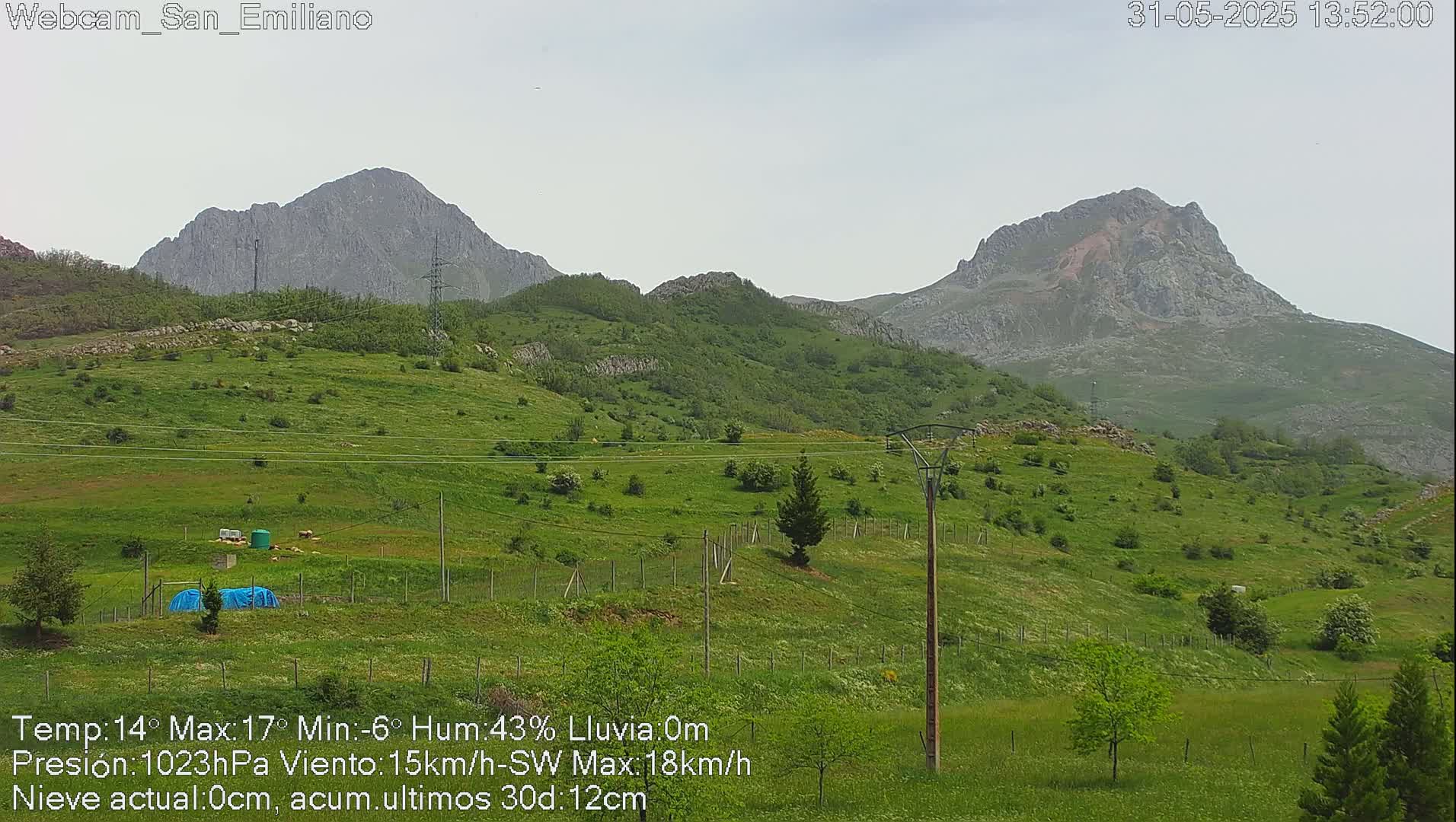 A green, hilly landscape with rocky mountains in the background under an overcast sky.