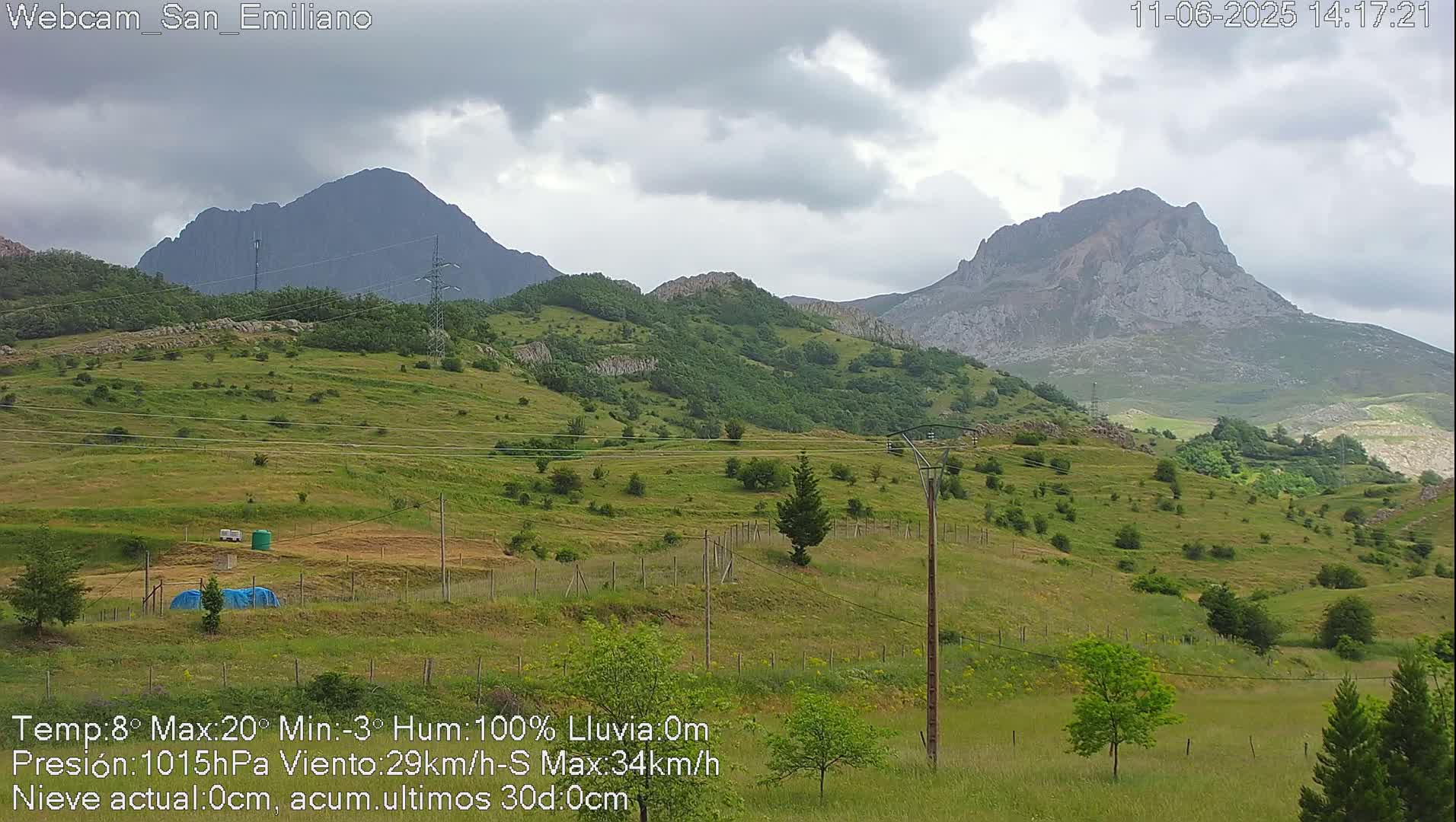 A green, hilly landscape under a cloudy sky features two prominent mountains in the background.