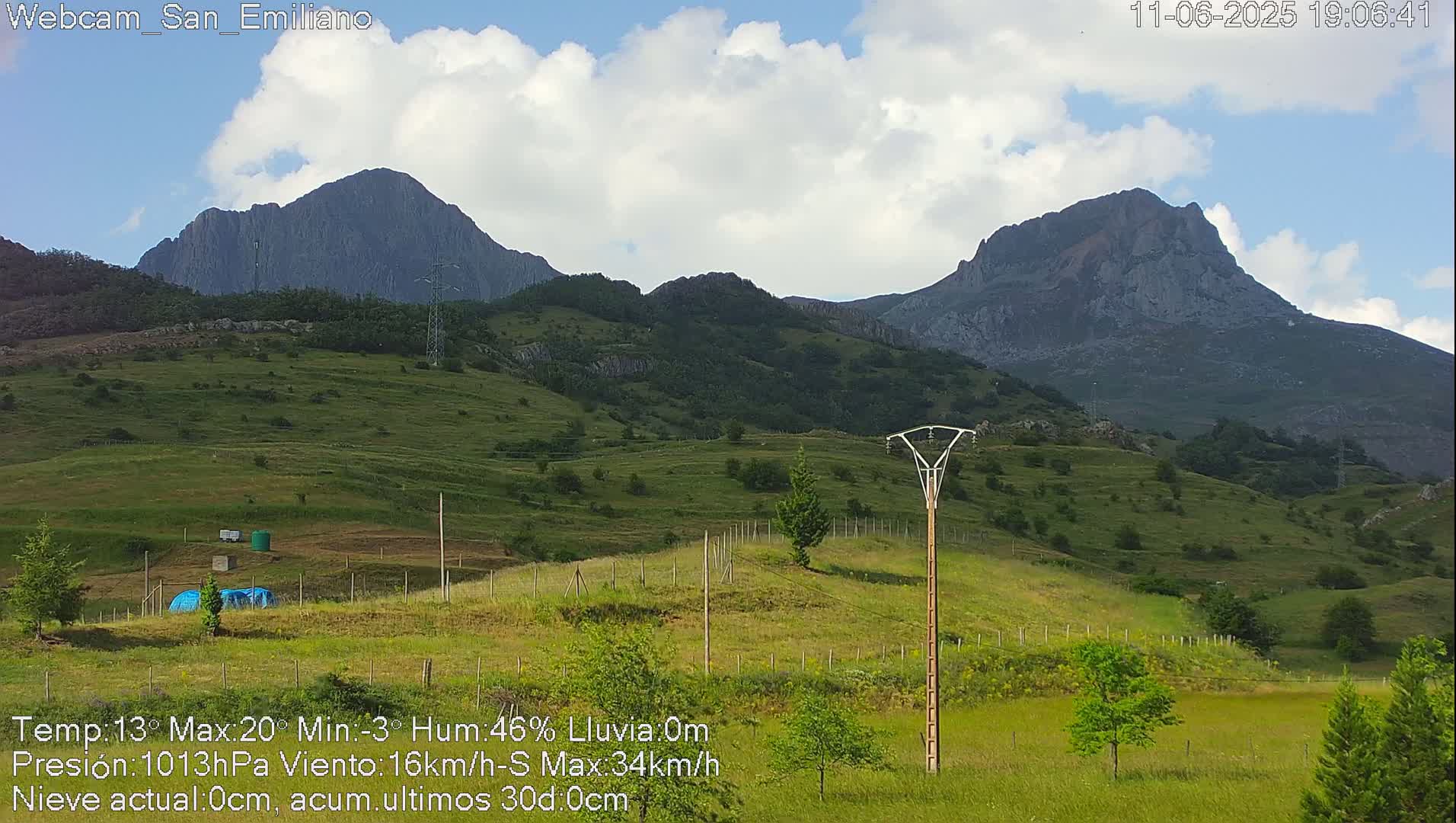 Rolling green hills and two prominent mountains are visible under a partly cloudy sky.
