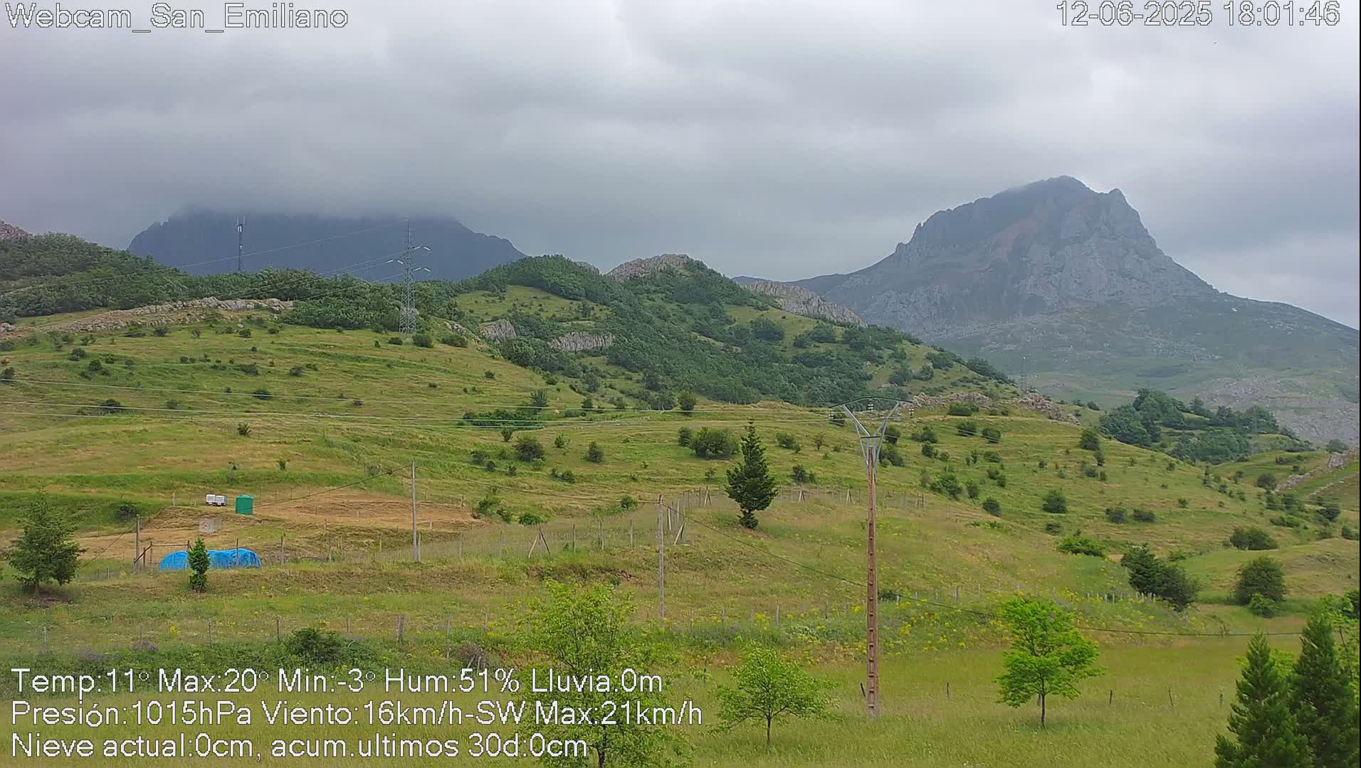 A view of rolling green hills and mountains under a cloudy sky.