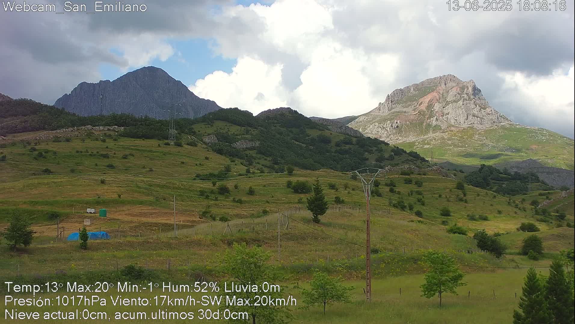 Two mountainous peaks are visible under a partly cloudy sky, with green hills and sparse vegetation in the foreground.
