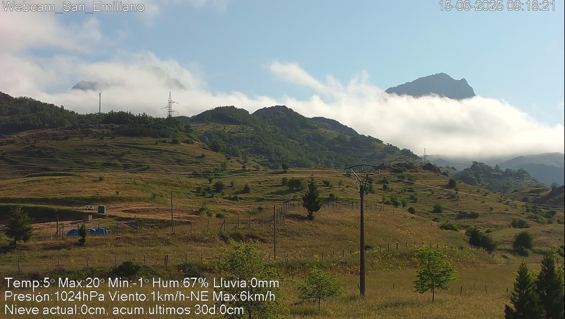 Rolling hills with low-lying clouds partially obscuring distant mountains under a mostly clear sky.
