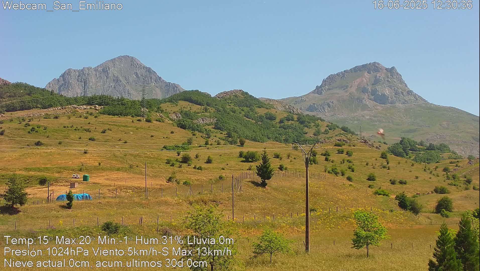 A sunny view of rolling hills and mountains, with some sparse vegetation and utility poles visible.