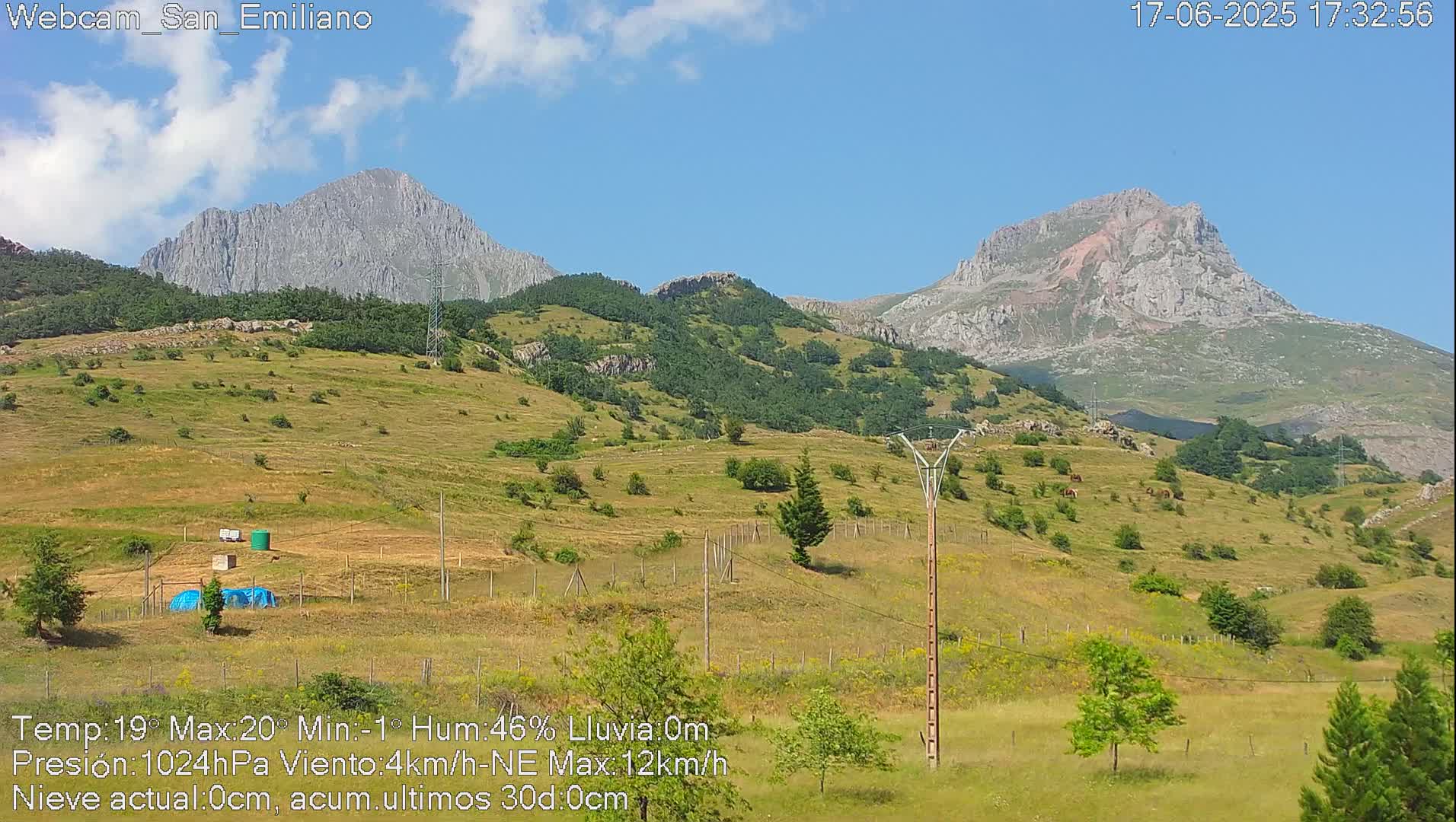 A sunny, clear day reveals rolling green hills and distant, rocky mountains under a mostly blue sky.