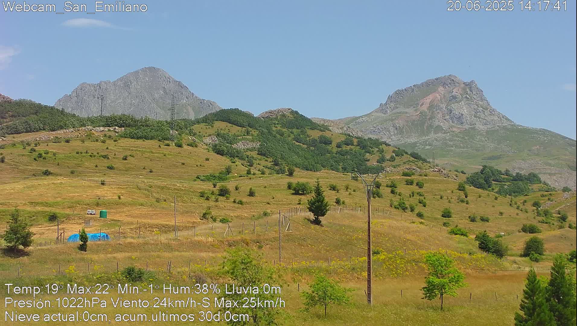 A sunny, hilly landscape with two prominent mountains in the background, under a clear blue sky.