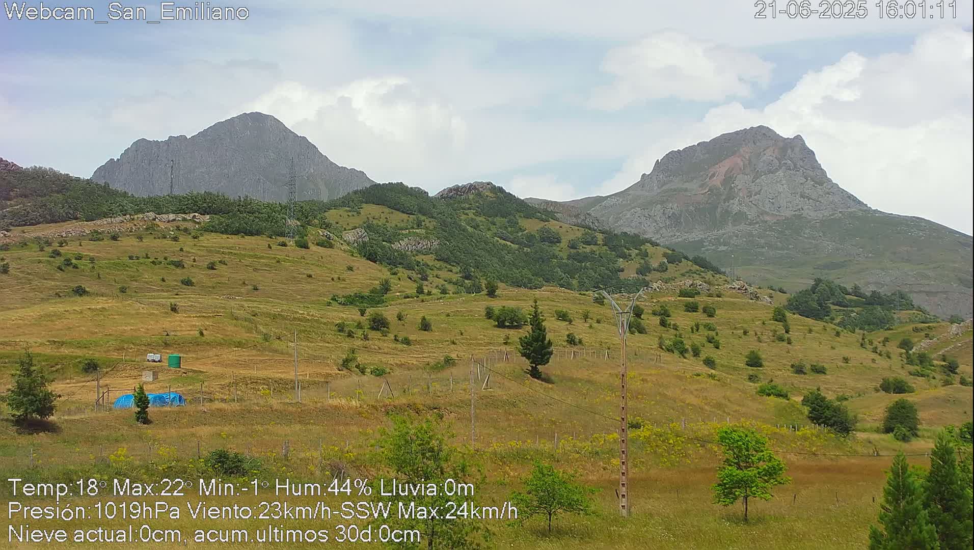 A partly cloudy day reveals rolling hills dotted with sparse vegetation and two prominent mountains in the background.