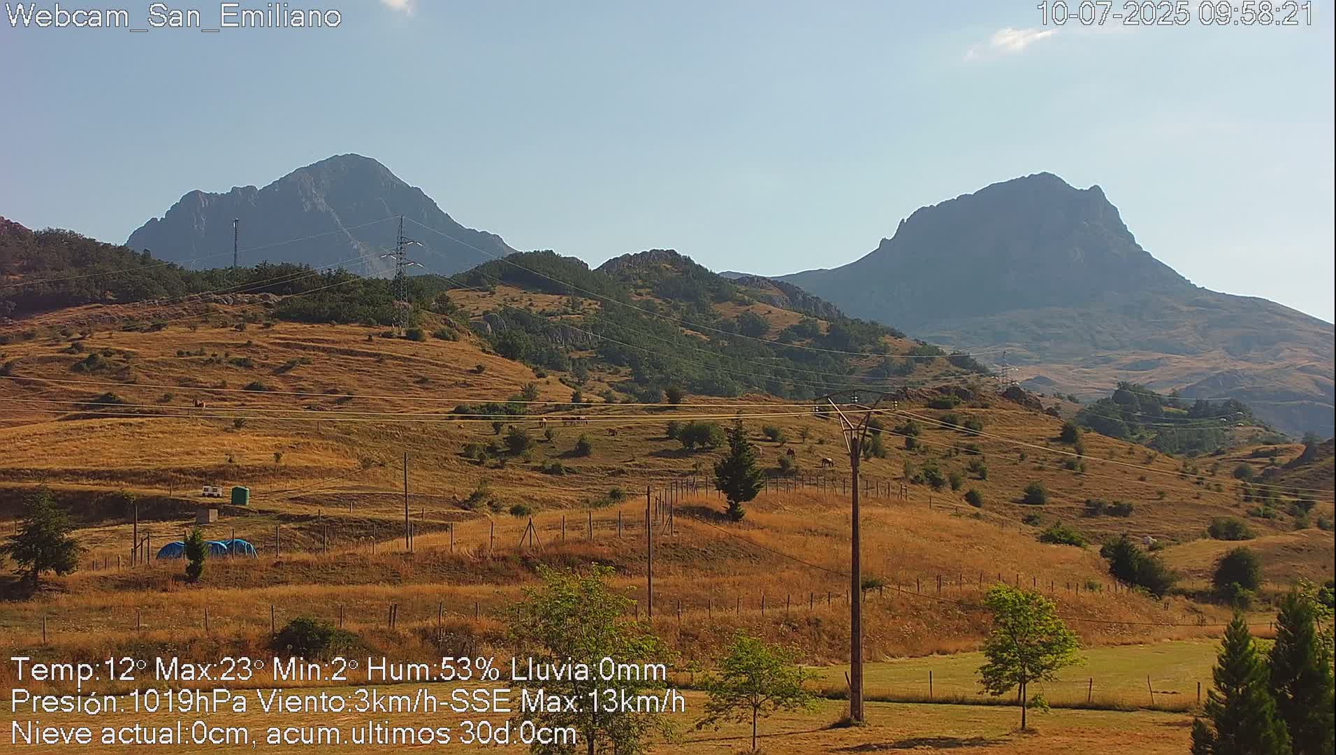A dry, sunny landscape with rolling hills and mountains in the background, under a clear sky.