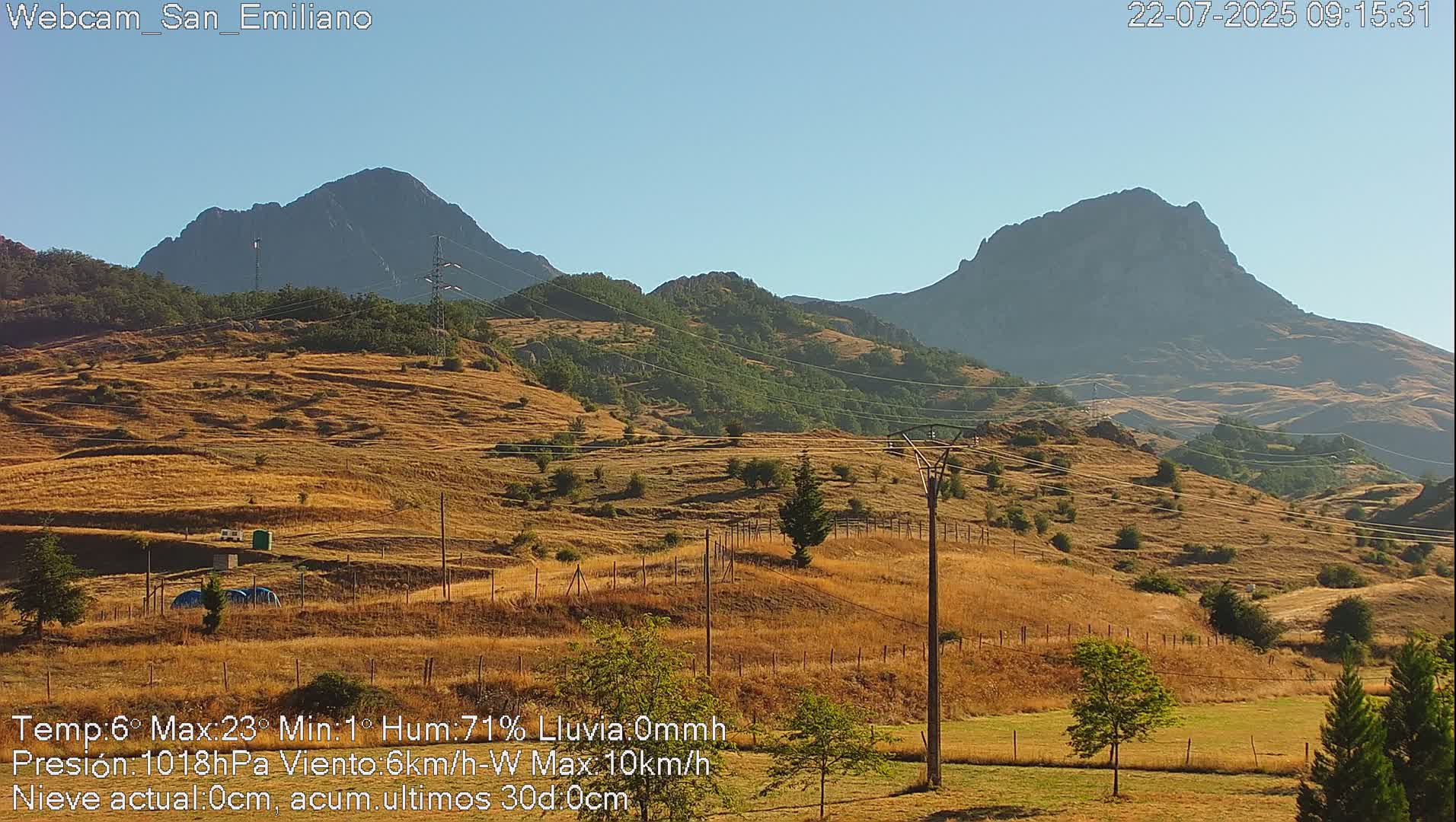 A sunny, dry landscape of rolling hills and distant mountains under a clear blue sky.