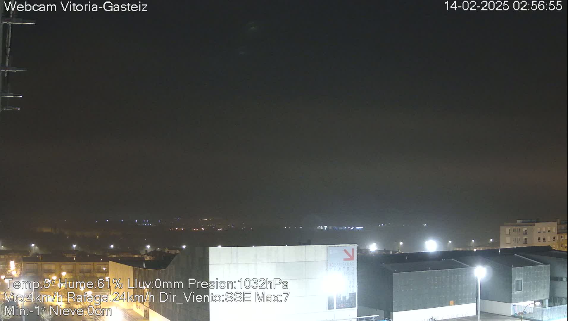 A nighttime view of a city shrouded in fog or haze, with lights illuminating buildings and a flat expanse in the distance.