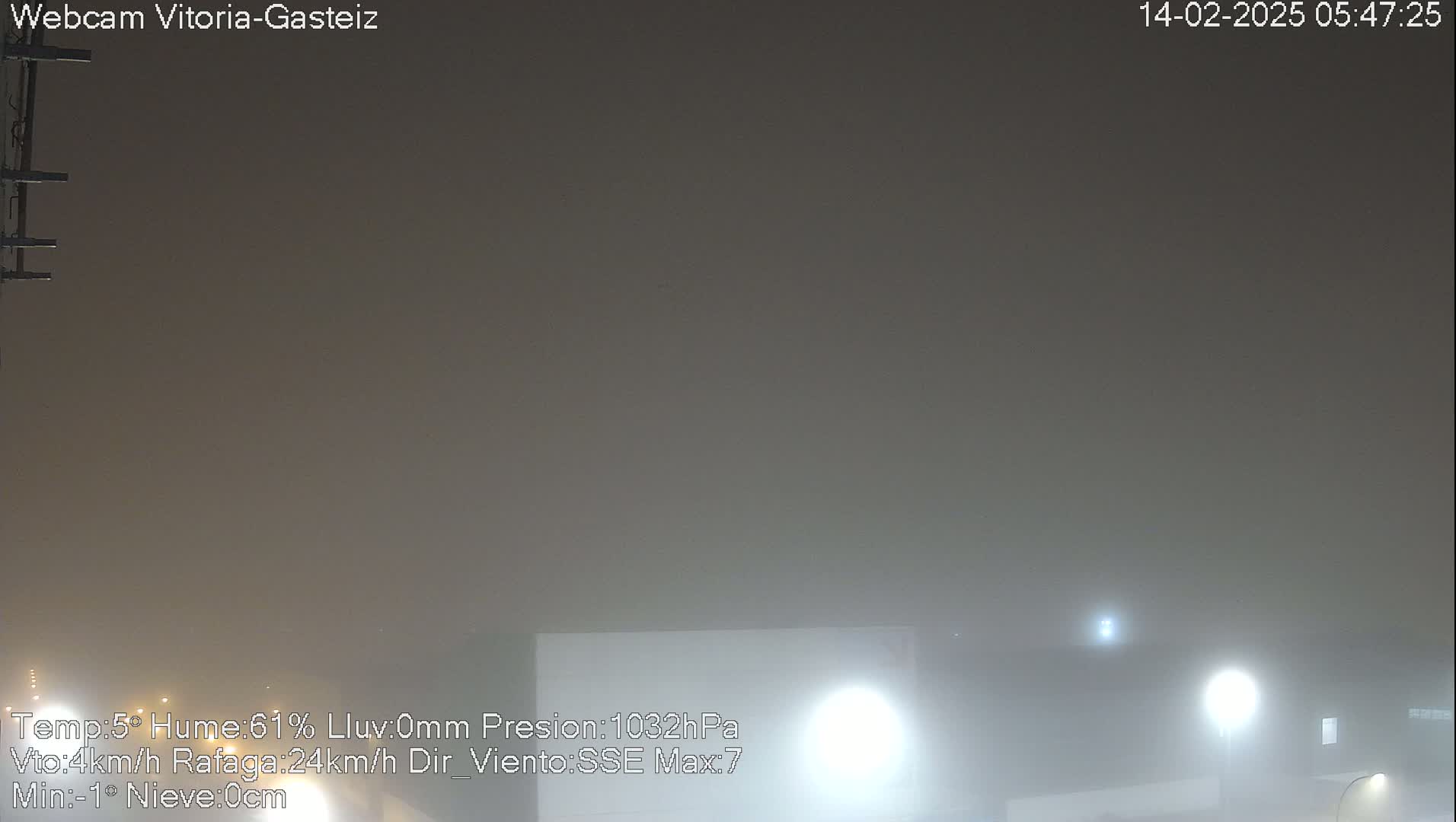 A foggy, dimly lit outdoor scene at night shows a building and lights partially obscured by heavy fog.