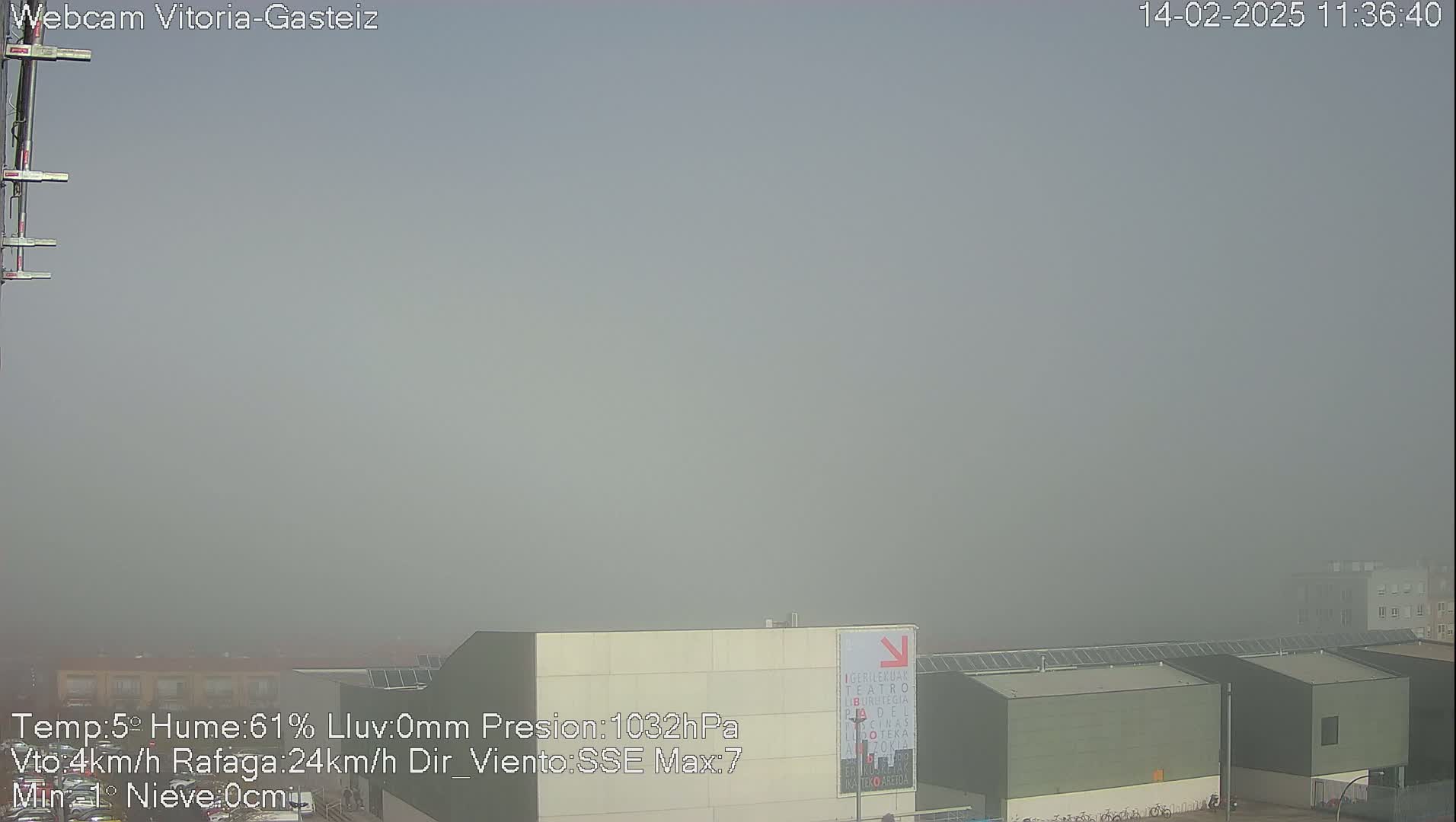 A foggy, outdoor scene shows several low buildings with flat roofs under a hazy sky.