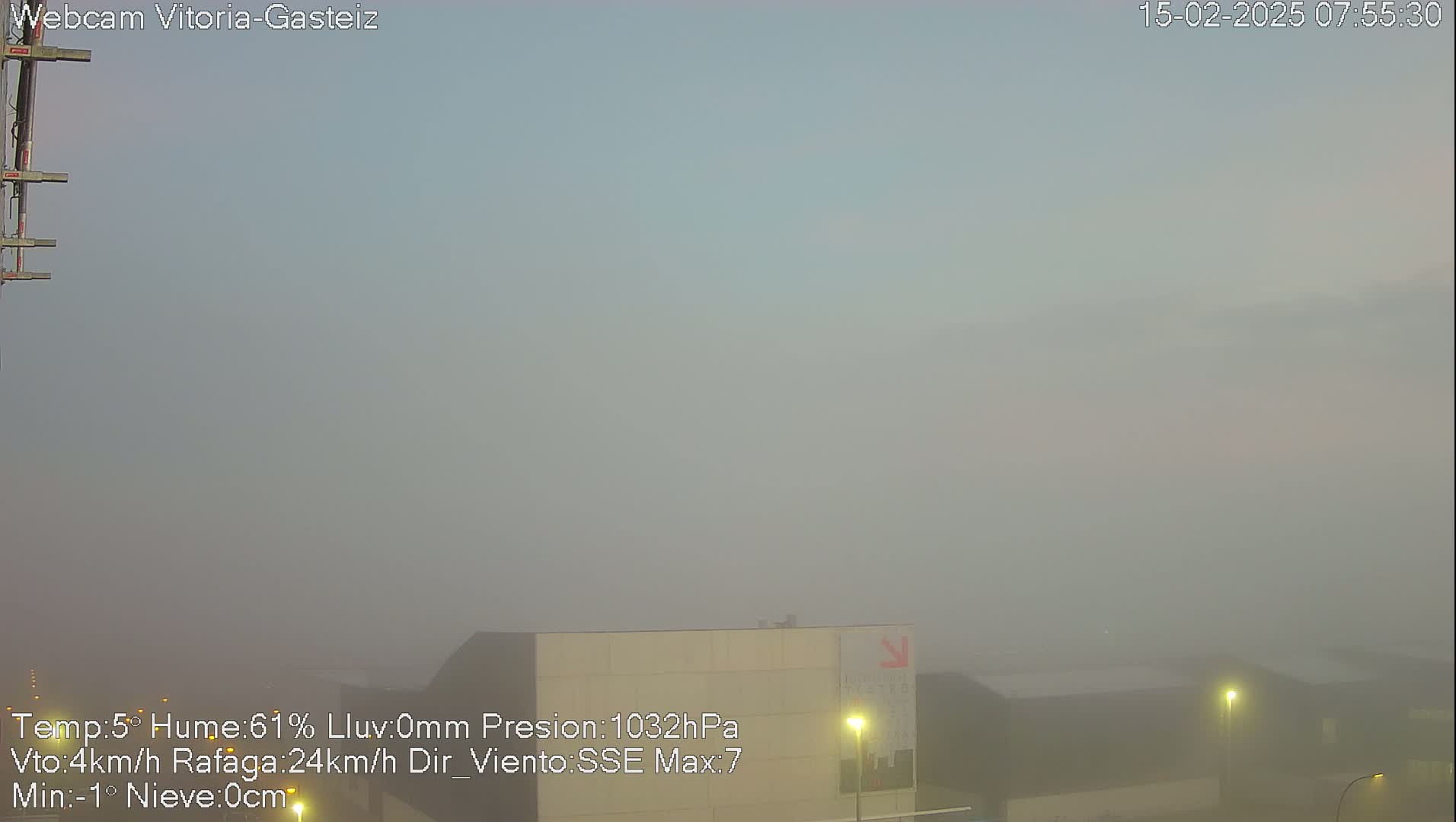 A foggy, low-visibility scene shows a flat expanse with a building and some lights visible in the distance.