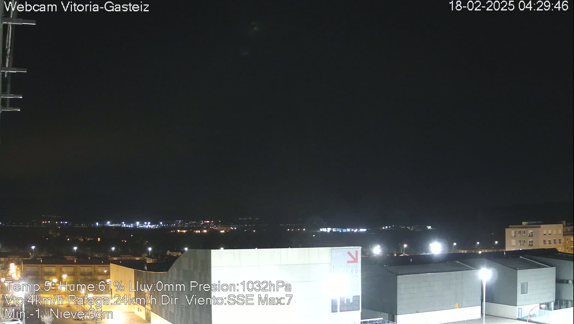 A nighttime view of a city skyline under a dark, clear sky, with lights illuminating buildings and a distant horizon.