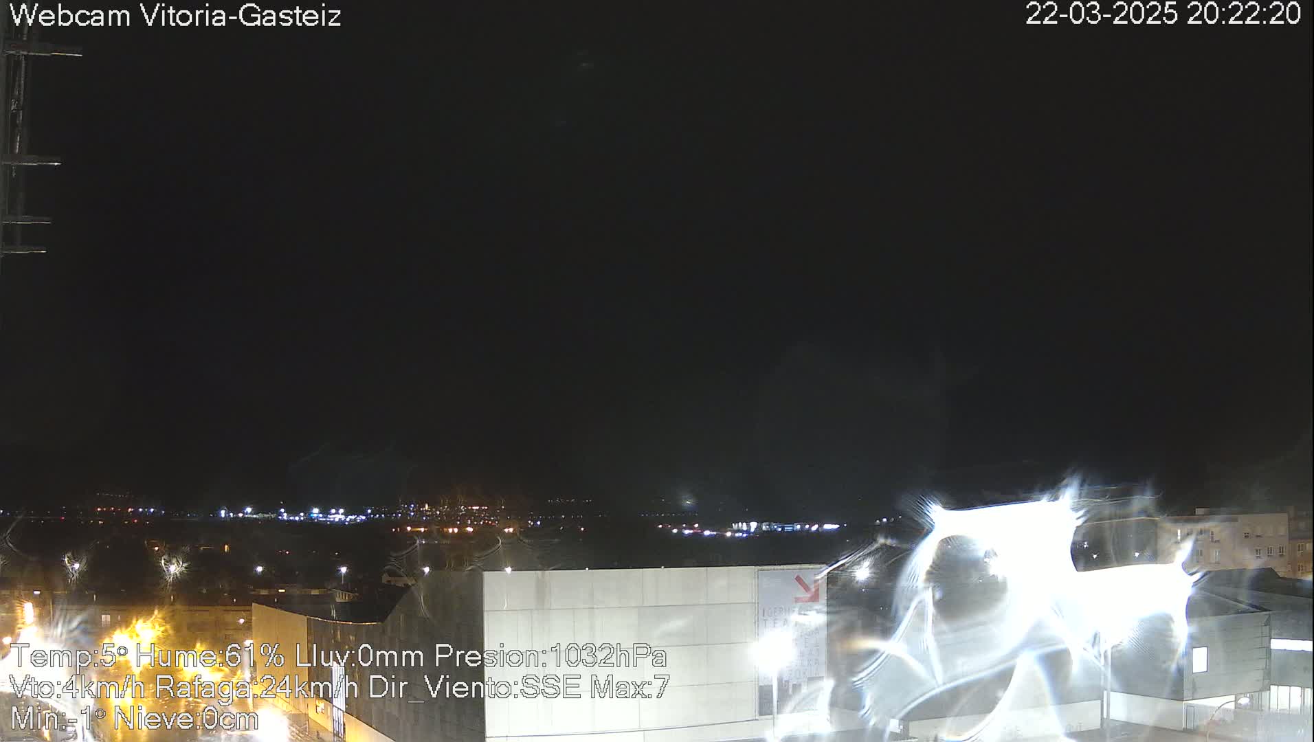A nighttime view of a city illuminated by lights under a dark sky with some lens flare.