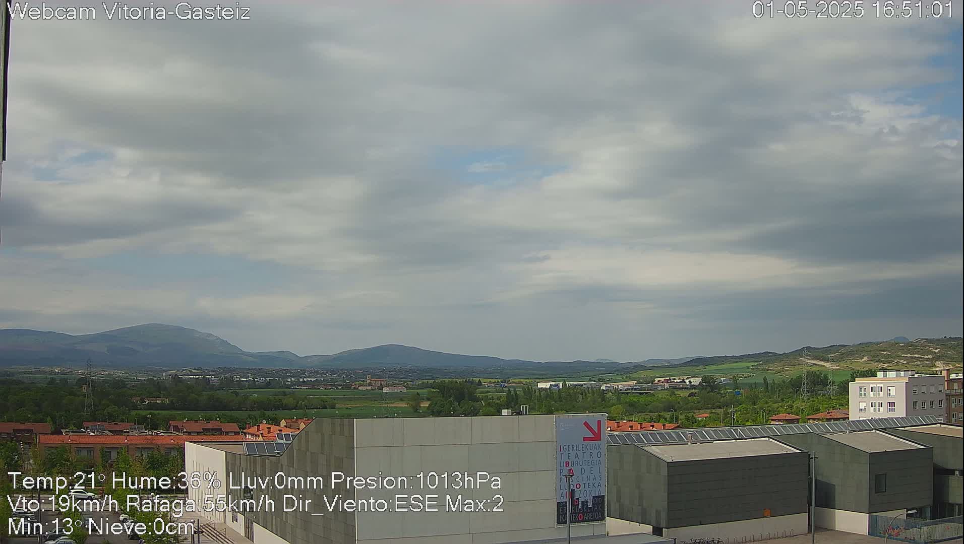 A partly cloudy sky overlooks a suburban landscape with low-lying hills in the distance.