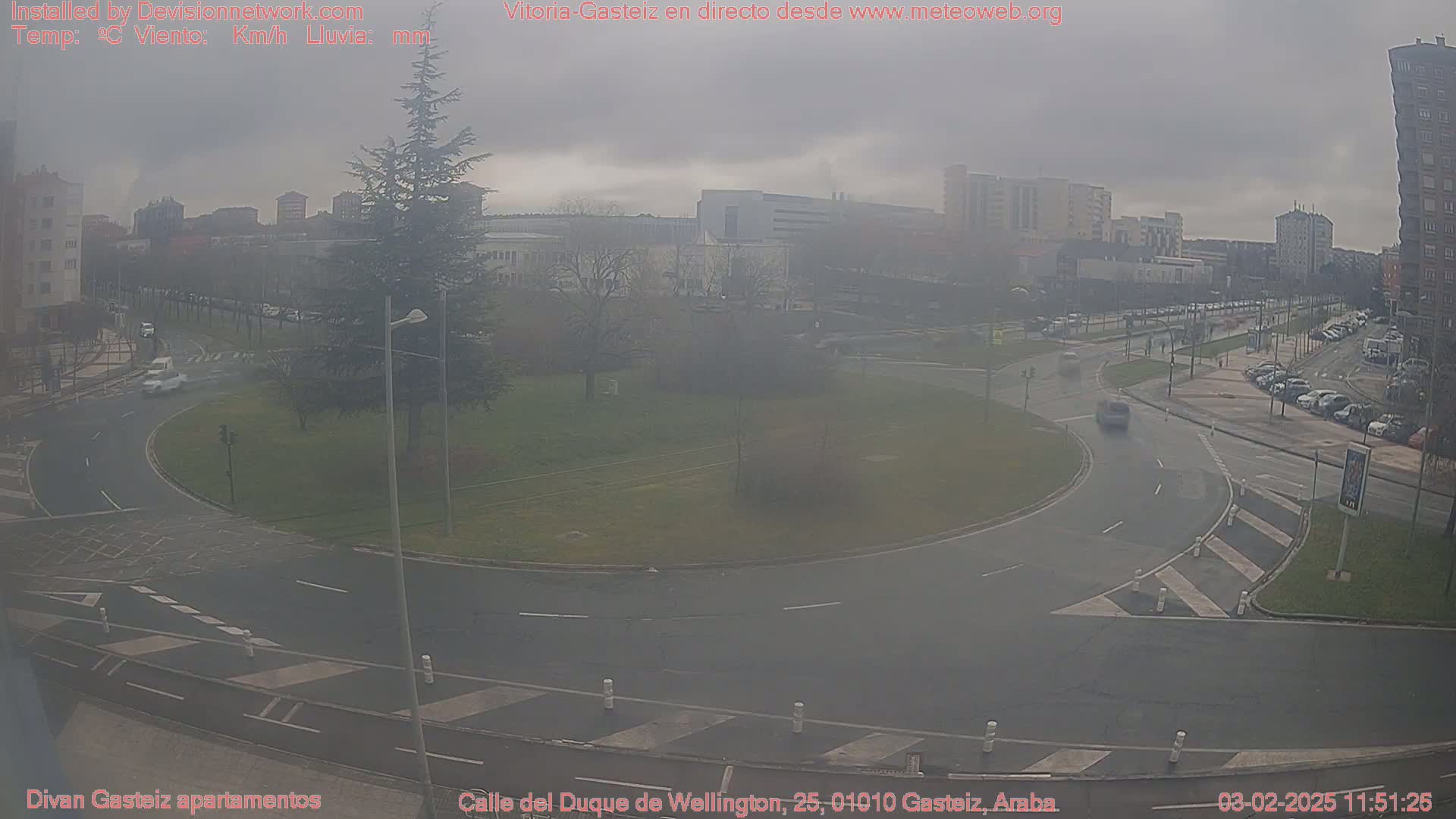 A hazy, overcast view of a roundabout in a city, with several cars visible and buildings in the background.