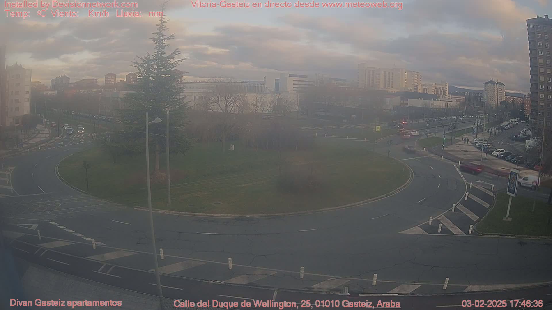 A hazy, overcast day shows a roundabout in a city with sparse traffic and several buildings in the background.