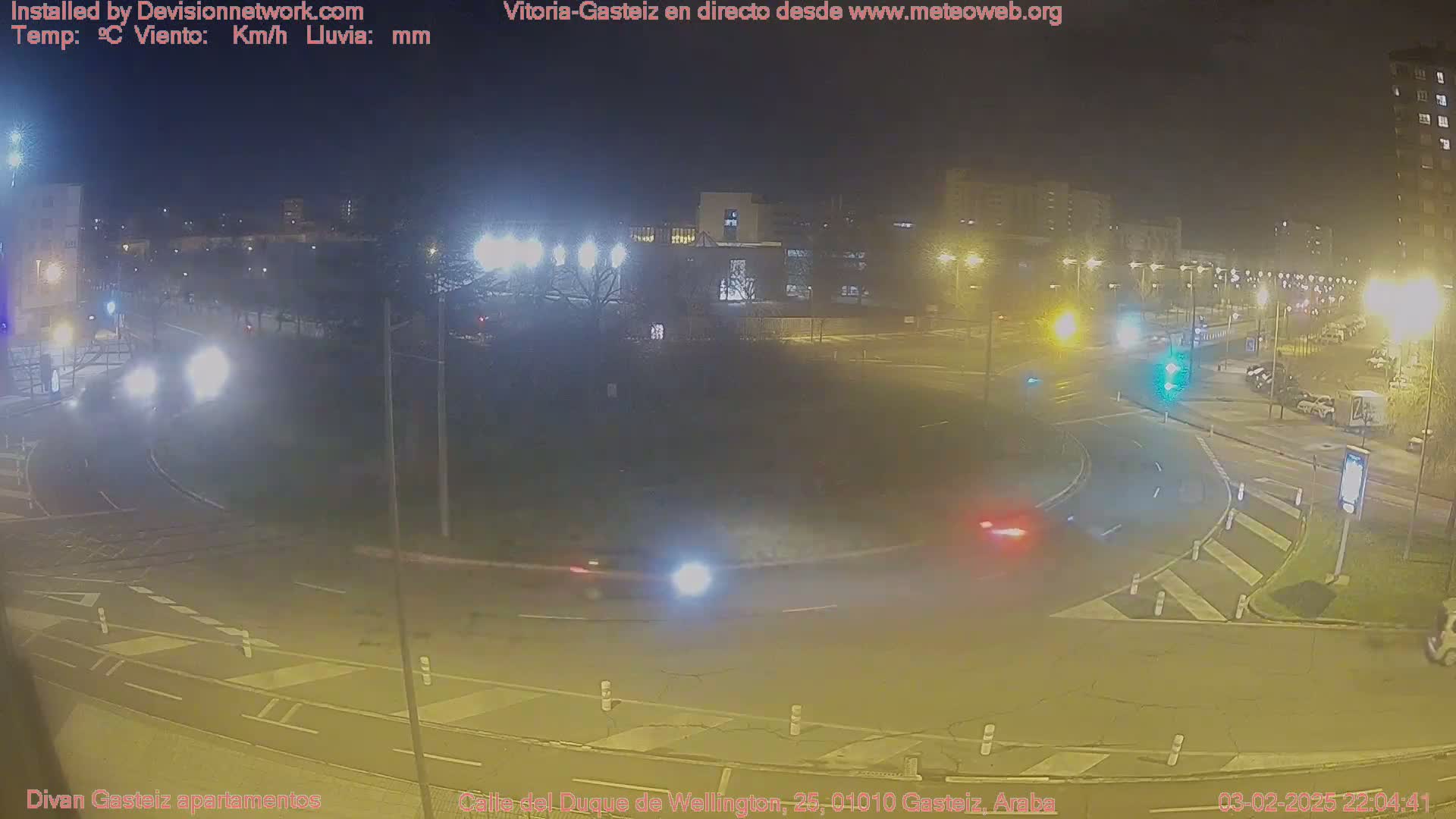 A nighttime view of a roundabout with several cars, illuminated by streetlights under a clear, dark sky.