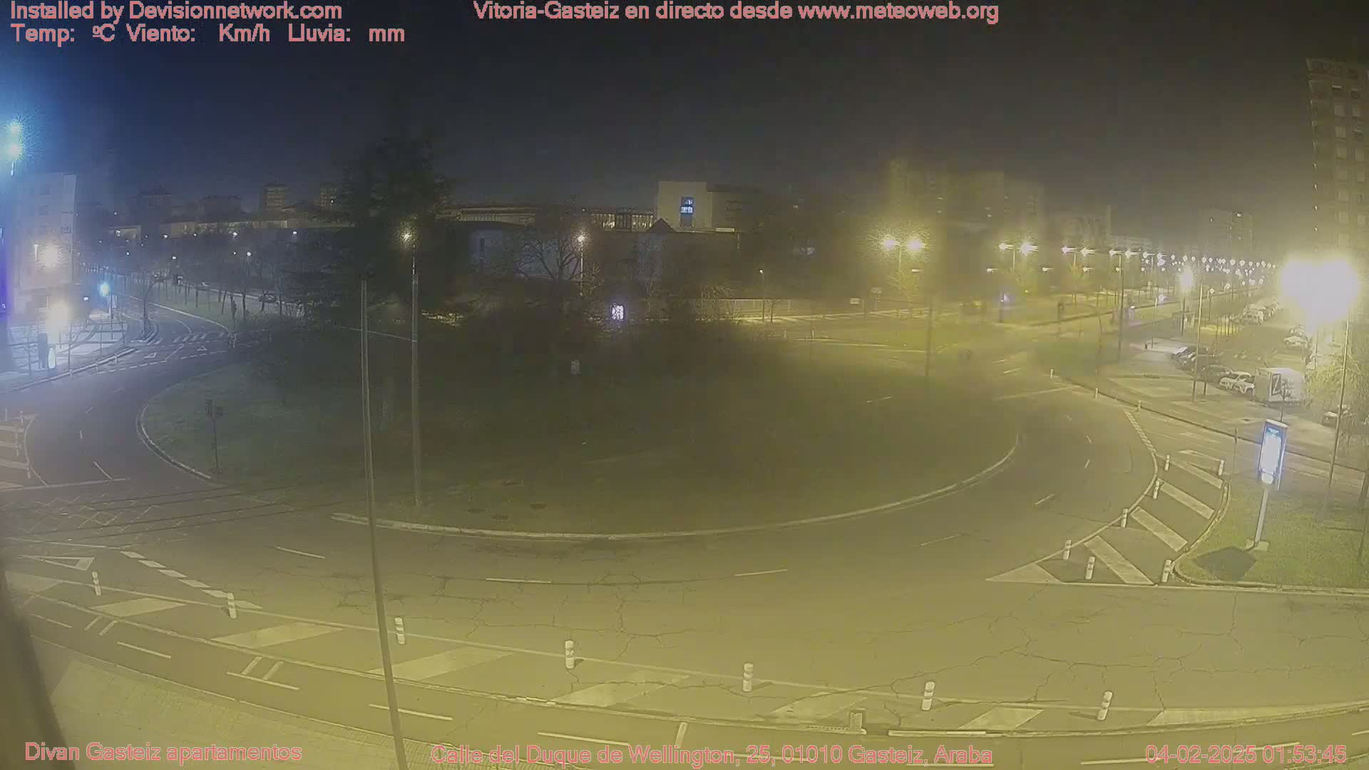 A nighttime, hazy view of a roundabout and surrounding streets, illuminated by streetlights.