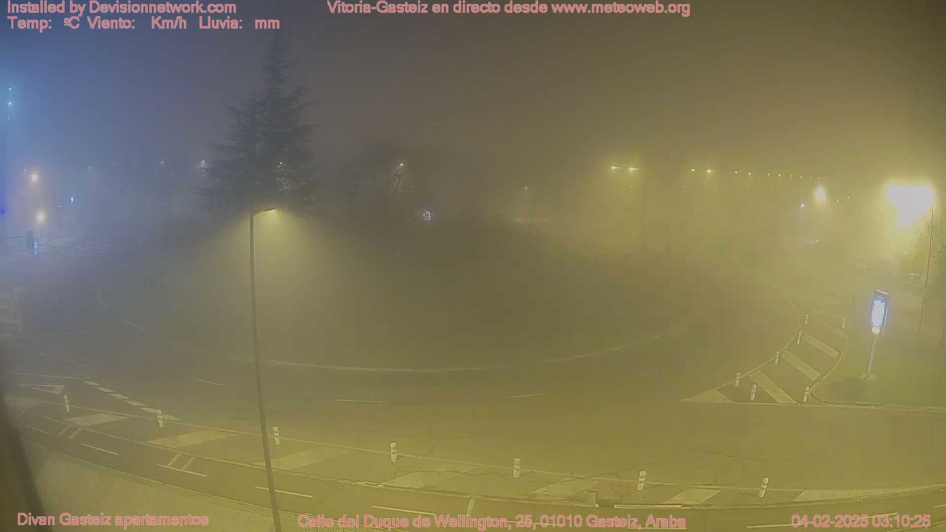 A foggy night scene shows a road intersection with streetlights and a lone tree, illuminated in a yellow-tinged haze.
