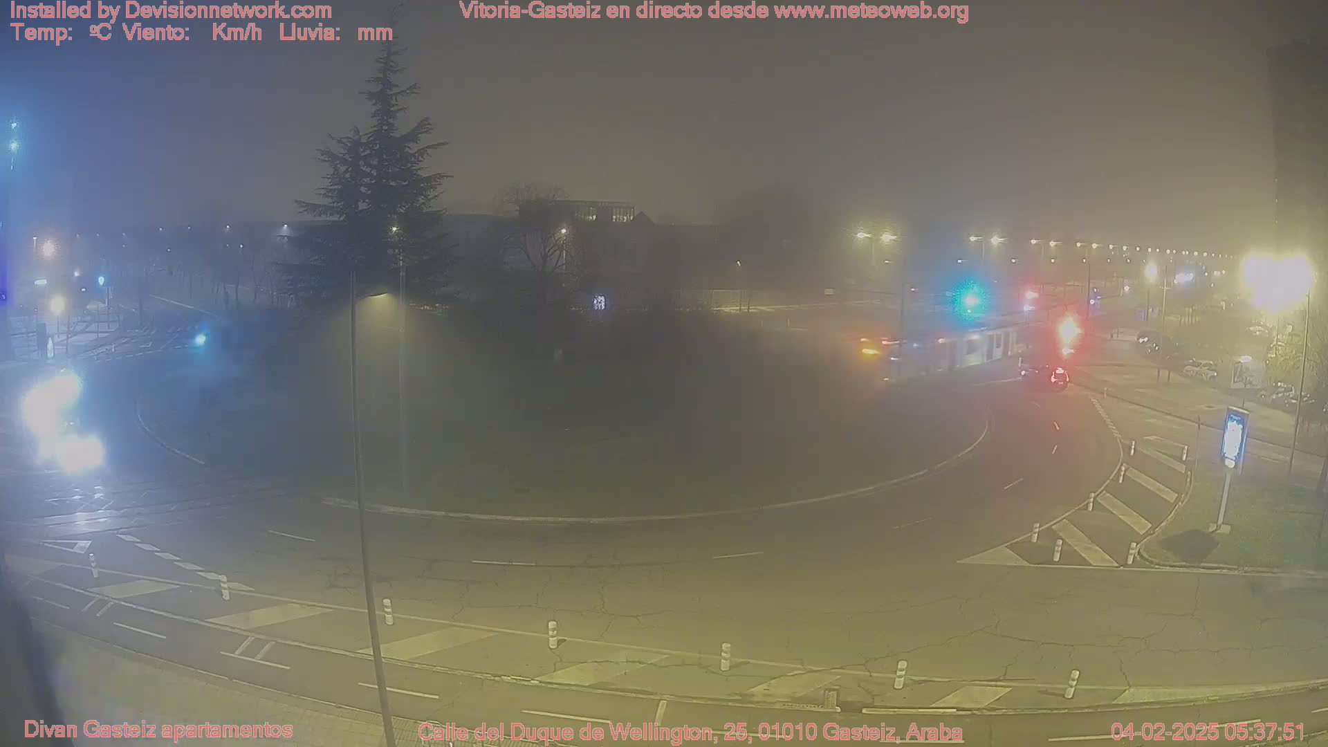 A nighttime view of a foggy roundabout with several cars and streetlights.