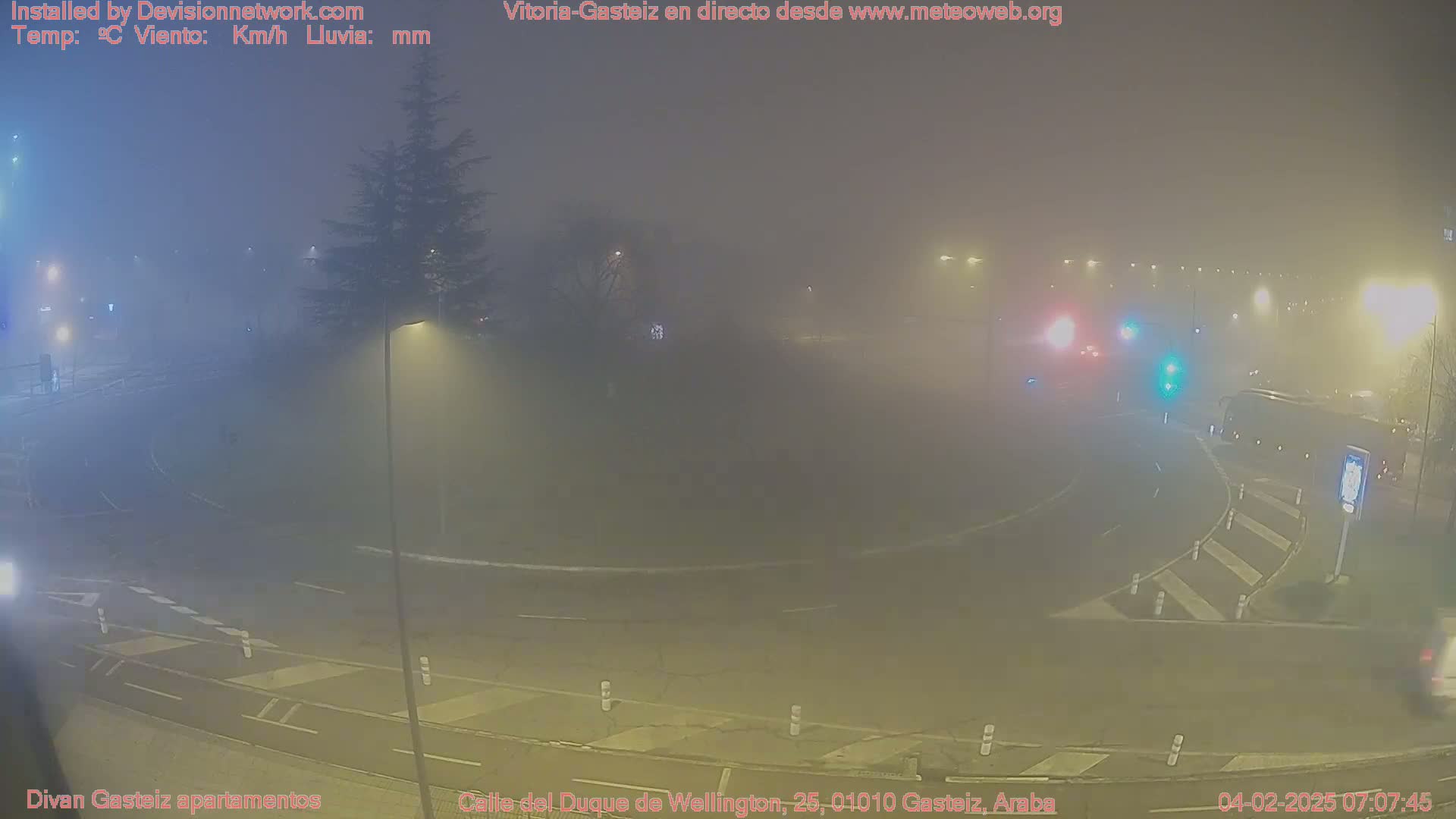 A foggy night scene shows a roundabout with streetlights, vehicles, and pedestrian crossings.