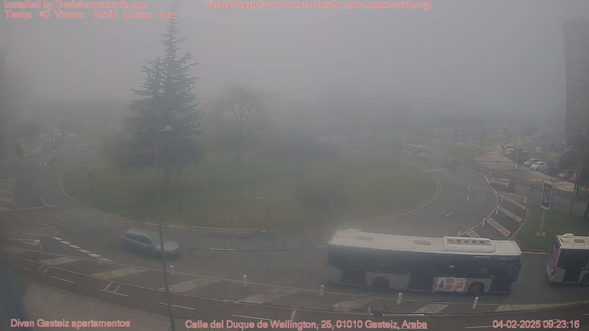 A foggy roundabout with a bus and several cars is visible, surrounded by muted greenery and buildings.