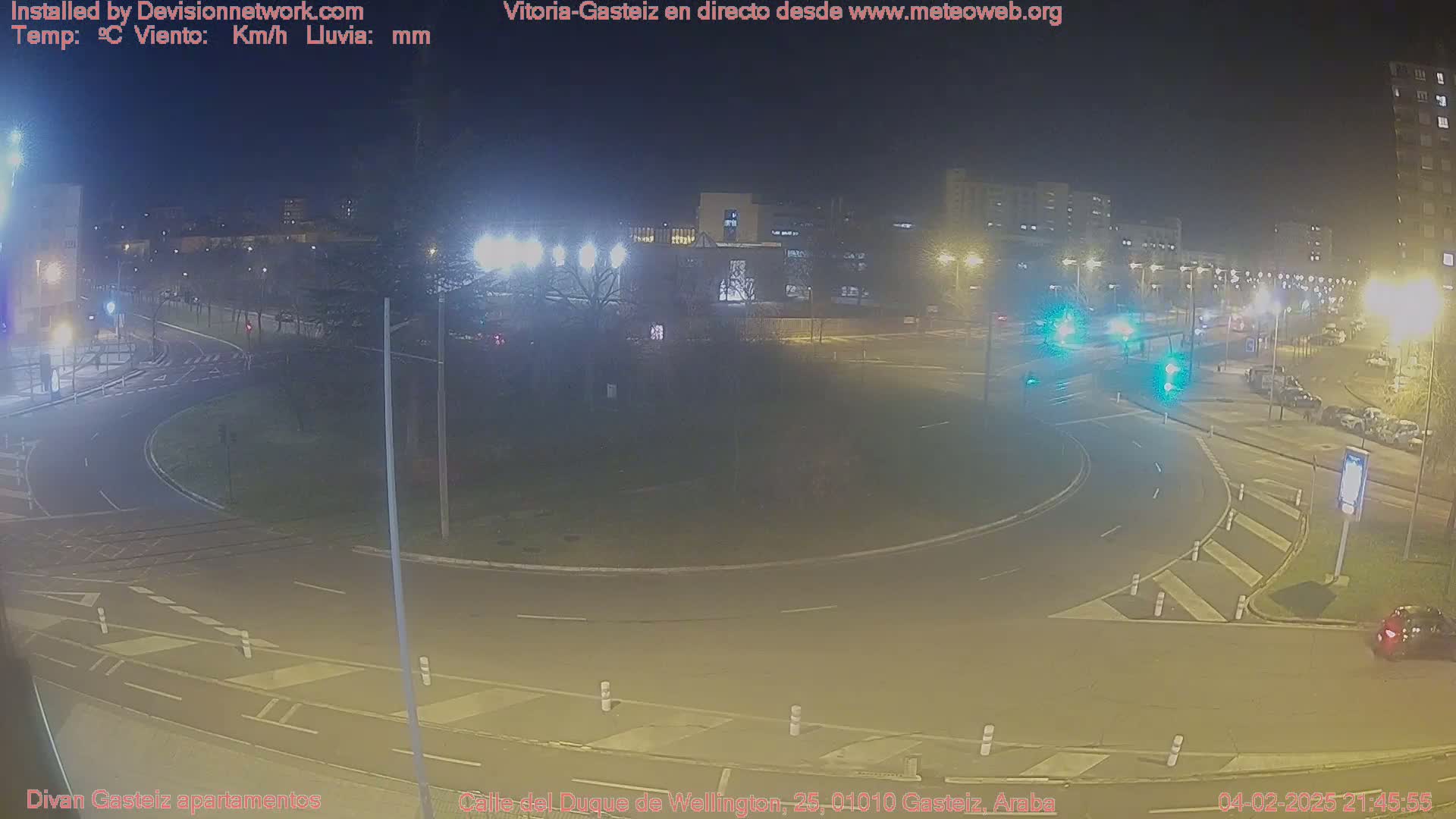 A nighttime view of a roundabout with sparse traffic and streetlights illuminating the surrounding buildings and trees.