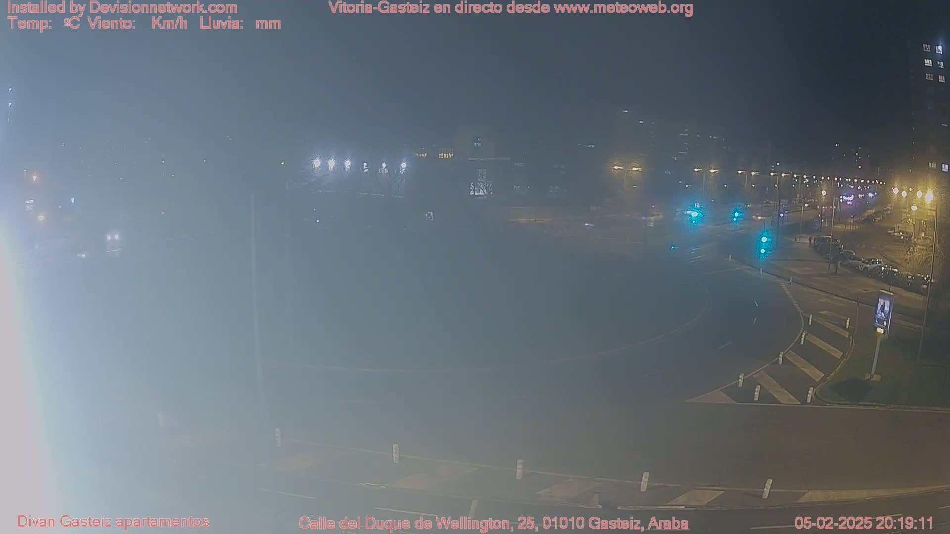 A nighttime, foggy view of a roundabout with several cars and streetlights.