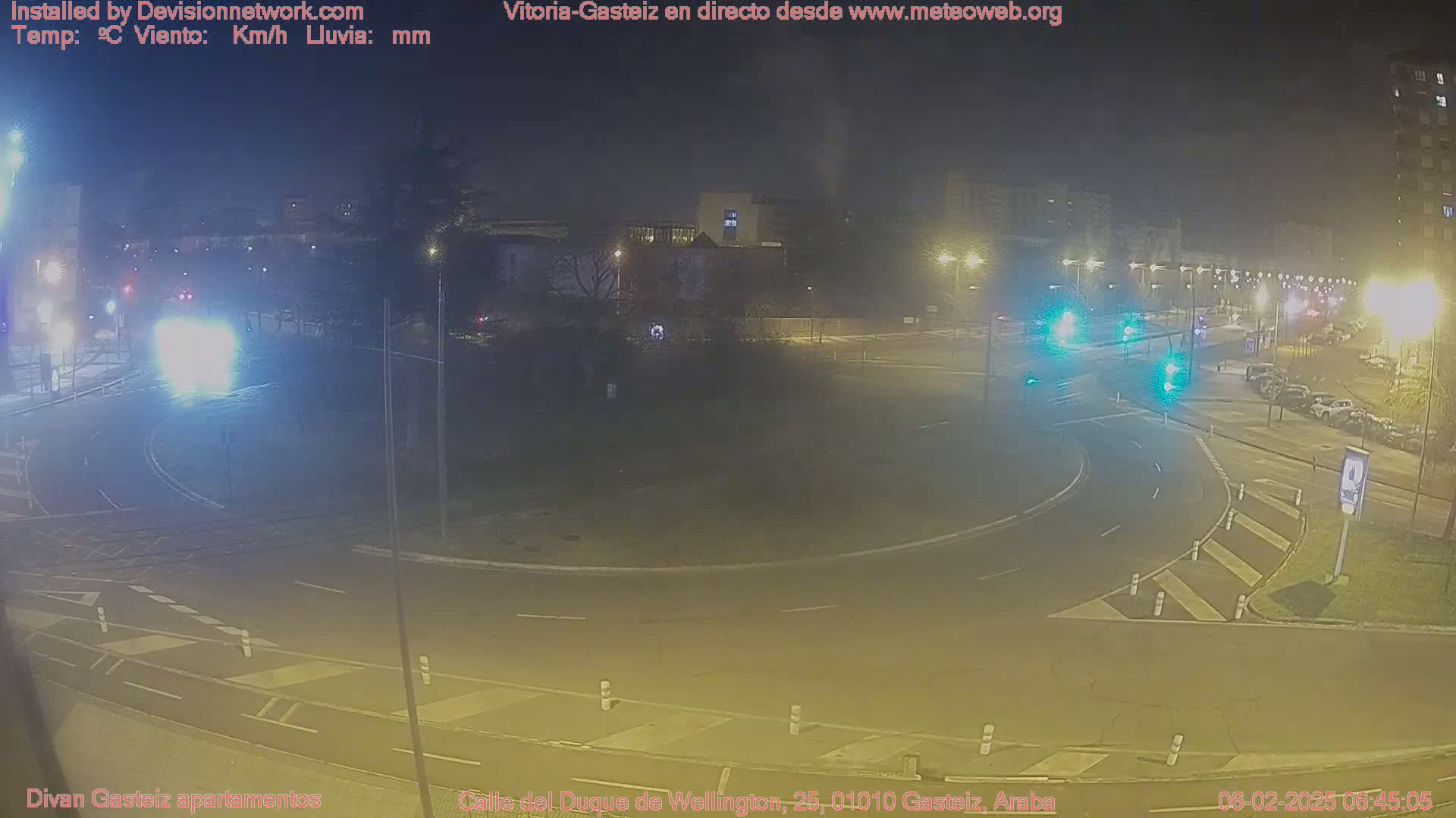 A nighttime, dimly lit roundabout with cars and streetlights, under overcast skies.